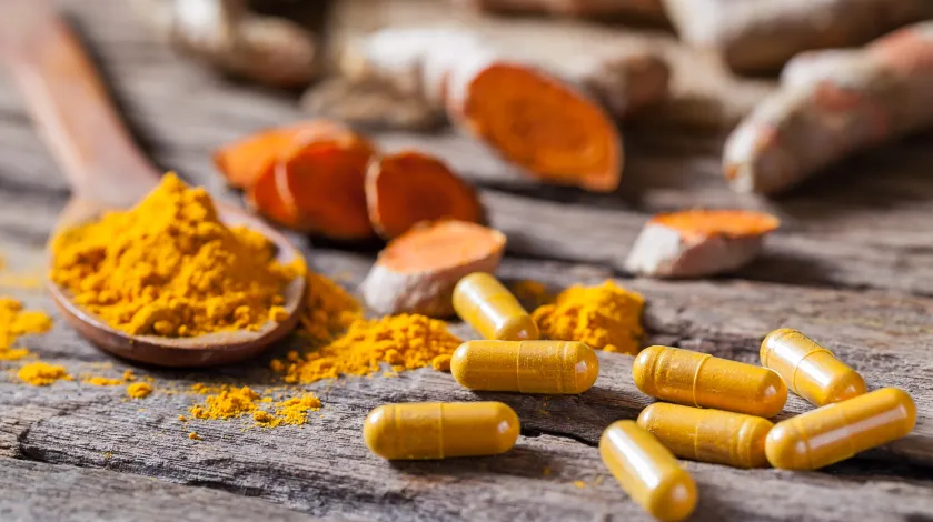 Turmeric powder on a wooden spoon pictured next to several turmeric supplement pills